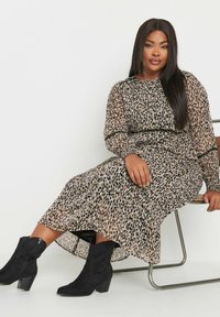 Leopardi kuvioitu mekko beigen ja mustan läpikuultavan kankaan yhdistelmässä, pitkät hihat joustavilla hihoilla, yhdistetty mustiin nilkkasaappaisiin ja tuoliin.