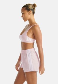 Jasnoróżowy sportowy stanik i pasujące krótkie spodenki. Stanik ma okrągły dekolt i trzy białe paski. Spodenki posiadają elastyczny pas.
