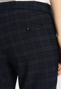 Marinblå rutiga byxor med en slät textur, med en bakficka och en svart knäppning. Mönstret består av mörkgröna och svarta linjer.