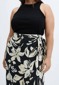Top senza maniche a coste nere abbinato a una gonna nera fluida con un motivo floreale bianco e dettaglio con fiocco laterale.