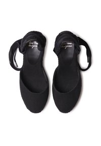 Scarpe in tessuto nero con punta rotonda, lati aperti e cinturino alla caviglia. L'interno presenta un'etichetta con il logo; l'esterno ha una texture liscia.