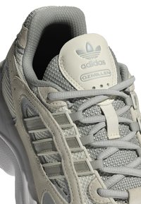 Szare sportowe sneakersy wykonane z siateczki i skóry, z wyściełanym kołnierzem, wyraźnym logo Adidas oraz charakterystycznymi teksturowanymi akcentami.