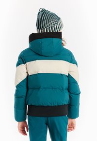 Tyrkysová puffrová bunda s krémovými a čiernymi pruhmi, s kapucňou a rebrovanými manžetami, doplnená o zodpovedajúce tyrkysové nohavice a pruhovanú pletenú čiapku.