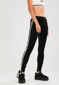 Svarta sammetstights med flätade spetsdetaljer längs sidan, designade för en figursydd form, i kombination med svarta platåskor.