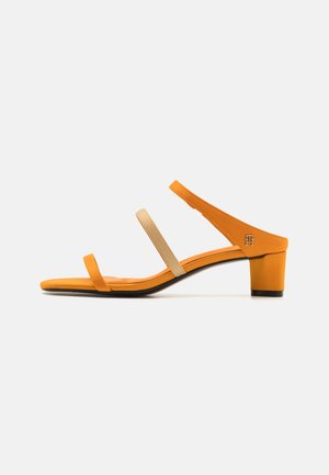 Sandalias abiertas de punta cuadrada en tonos naranja y beige, con dos tiras estrechas y tacón cuadrado. Textura suave con un diseño minimalista.