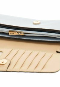 Portafoglio beige con una tasca con zip dotata di una cerniera dorata contrassegnata "GUESS", e più slot per carte con una finitura texturizzata.