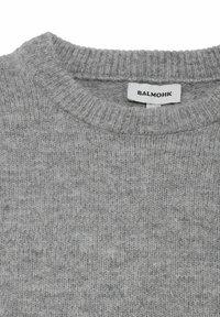 Grijze gebreide trui met een geribde ronde hals. De stof heeft een zachte, textuurachtige uitstraling. Inclusief een label met "BALMOHK" erop gedrukt.