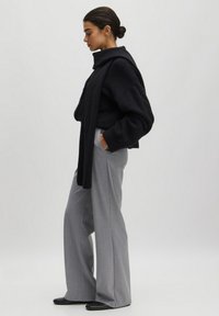 Schwarzer, übergroßer Pullover mit Schalkragen, kombiniert mit hellgrauen, weiten Hosen. Einfarbige Töne, weicher Stoff und minimalistisches Design.