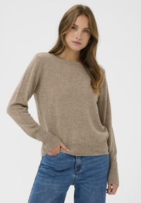Beżowy sweter dziany z okrągłym dekoltem, ściągaczami przy mankietach i u dołu. Połączony z niebieskimi dżinsami, oferującymi miękką teksturę i luźny krój.