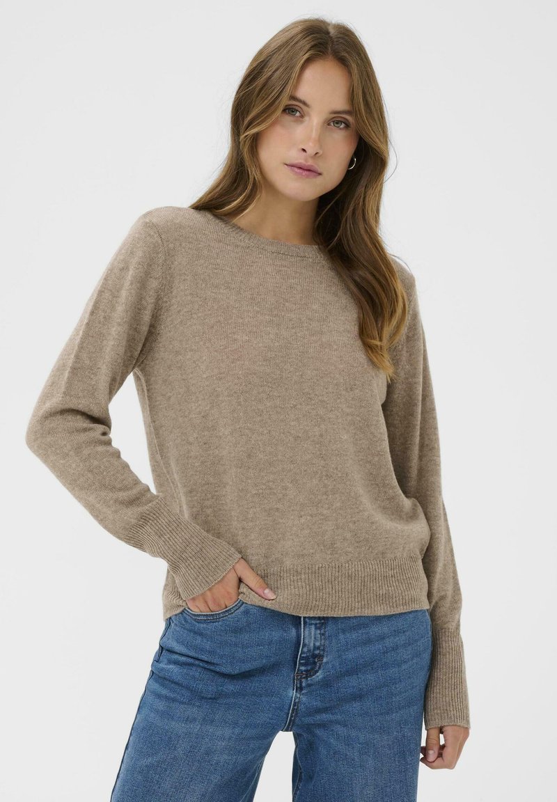 Beżowy sweter dziany z okrągłym dekoltem, ściągaczami przy mankietach i u dołu. Połączony z niebieskimi dżinsami, oferującymi miękką teksturę i luźny krój.