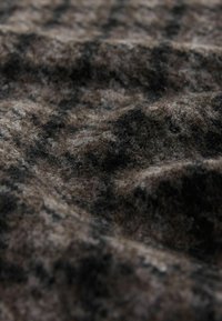 Braun- und schwarz gemusteter Stoff mit einer weichen, strukturierten Oberfläche, die ein fuseliges Aussehen und wellenartige Drapierungen aufweist.