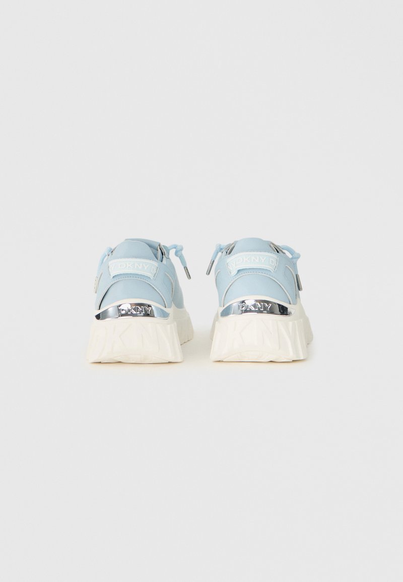 Sneakers azzurri chiari con suole bianche spesse, accenti argento "DKNY" e toppe del logo "DKNY" bianche sulle linguette posteriori, viste da dietro.