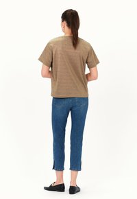 Metallisch goldenes T-Shirt mit kurzen Ärmeln und lockerer Passform, kombiniert mit schmalen blauen Jeans mit Schlitzsaum und schwarzen flachen Schuhen.