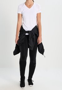 White v-neck sports shirt, black leggings with mesh panels, black jacket tied around waist, and black athletic shoes.