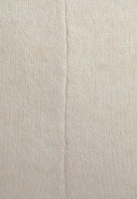 Licht beige gebreide stof met een zachte textuur; heeft een centrale naad die verticaal loopt; minimale contrasten.