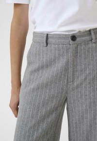 Close-up of a person wearing grey pinstriped trousers and a white t-shirt, showing waistline and a button detail.