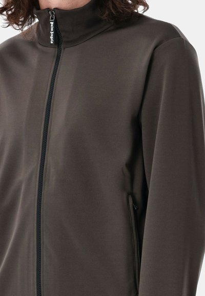 Giacca marrone con zip, colletto alto e due tasche laterali; tessuto morbido ed elastico con finitura opaca e dettagli di design minimi.