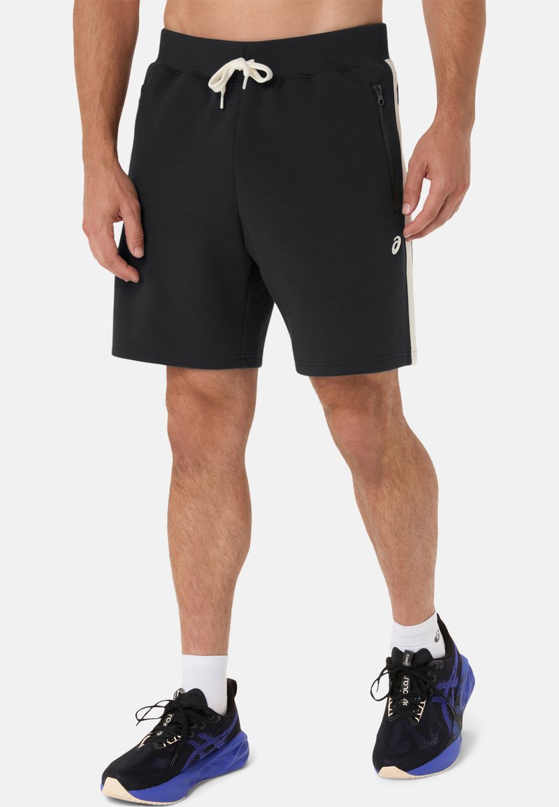 Shorts de sport noirs en tissu doux, avec une taille élastique à cordon de serrage, des poches latérales zippées et des bandes latérales contrastantes.