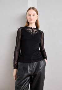 Haut noir à manches longues avec des détails en dentelle au niveau du col et des manches, associé à un pantalon en cuir noir taille haute.