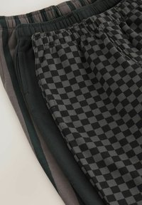 Drei Paar Jogginghosen ausgestellt. Die Farben umfassen Schwarz mit grauem Karomuster, Dunkelgrün und gedämpftes Grau. Weicher Stoff mit elastischem Bund.