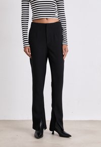 Höga svarta byxor med sidospalter, skräddarsydd design, slät textur, bärs med en svart och vit randig crop top och spetsiga klackar.