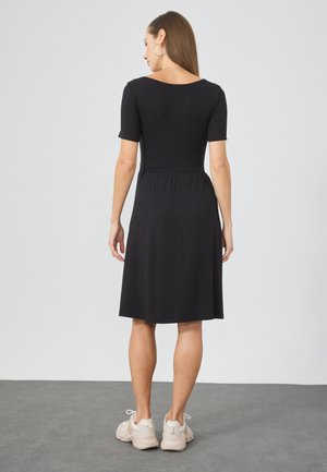 Black knee-length dress with short sleeves and a fitted bodice, featuring a gathered waist and soft fabric; paired with light-colored sneakers.