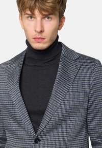 Szary i niebieski blezer w wzór houndstooth o dopasowanym kroju, z wyłógami i guzikiem, noszony na czarnym swetrze z golfem.
