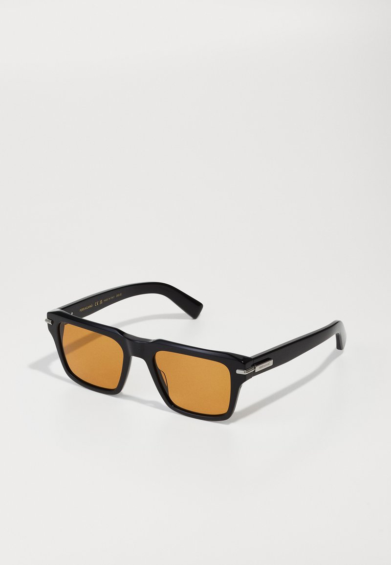 Lunettes de soleil rectangulaires noires avec des verres oranges, dotées d'une monture brillante et d'accents en métal argenté. Les branches texturées am�éliorent la prise.