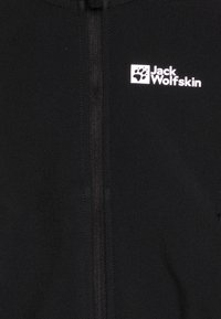 Melnā jaka ar pilna garuma rāvējslēdzēju, izgatavota no mīksta materiāla, ar baltu Jack Wolfskin logo kreisajā augšējā daļā.
