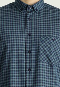 Camicia a quadri blu navy e verde con colletto classico, tasca anteriore e bottoni scuri, realizzata in un tessuto morbido.