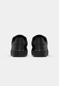 Sneaker neri con tomaia in pelle liscia, tacco arrotondato e una accentuazione dorata lungo la suola. Suola in gomma texturizzata per la presa.