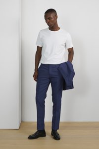 Camiseta blanca de manga corta combinada con pantalones navy ajustados y zapatos de vestir negros. Un blazer navy ajustado se sostiene en su mano derecha.