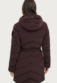 Cappotto imbottito bordeaux con motivo a zigzag, cintura elastica e cappuccio. Presenta una toppa nera sul maniche e una texture elegante e liscia.