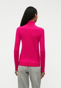 Fitted pink turtleneck sweater made of soft fabric, featuring long sleeves and a ribbed hem, paired with gray high-waisted jeans.