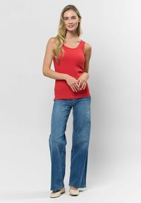 Červený žebrovaný top na ramínka s kulatým výstřihem, doplněný o světlemodré široké džíny a krémové ploché boty na neutrálním pozadí.