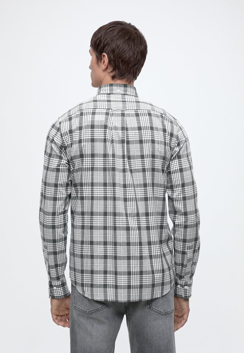 Mand iført en sort, hvid og grå ternet langærmet skjorte og grå jeans, set bagfra mod en ensfarvet baggrund.