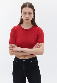 Maglione corto a maniche corte rosso con lavorazione a maglia testurizzata, scollatura rotonda e design aderente, abbinato a jeans neri a vita alta.