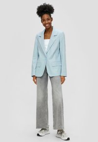 Blazer azzurro chiaro realizzato in un tessuto morbido, con revers a divergenza, chiusura a un bottone e due tasche frontali. Indossato con jeans grigi a gamba larga.