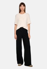 Beige cotton t-shirt with a textured graphic print, paired with black wide-leg trousers featuring a drawstring waist and side slits.