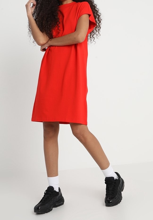 Robe rouge à manches courtes avec une coupe décontractée, fabriquée en tissu lisse. Portée avec des baskets noires et des chaussettes blanches pour un look décontracté.