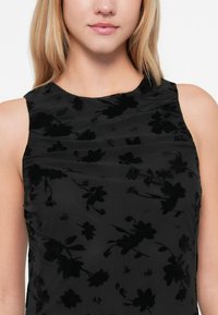 Zwarte tanktop met een bloemenvelours patroon en gestructureerde stof. Beschikt over een ronde hals en subtiele plooien voor extra detail.