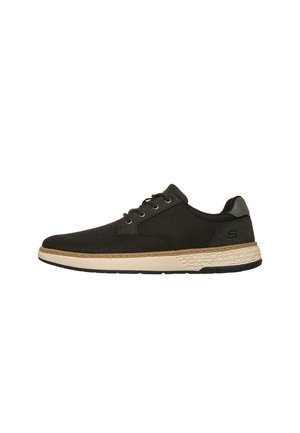 Zapatilla casual negra con cordones, suela beige texturizada y logo sutil en el talón, mostrada de lado sobre un fondo blanco.
