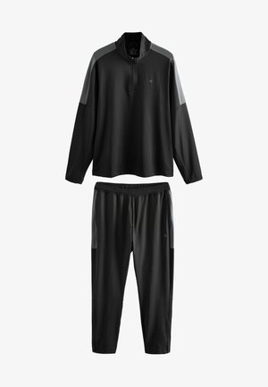 Schwarzer Sportanzug, bestehend aus einem langärmligen Oberteil mit Viertel-Reißverschluss und grauen Akzenten sowie passenden schmal geschnittenen Hosen mit elastischem Bund.