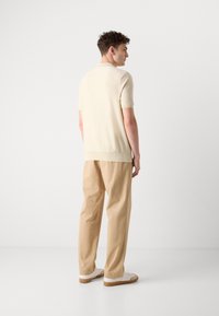 Kortärmad ljusbeige stickad tröja med rundad hals, kombinerad med beige vida byxor och vita sneakers med bruna sulor.