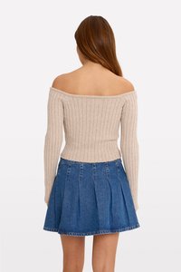 Top bej cu dungi, off-the-shoulder, purtat cu o fustă plisată din denim albastru. Topul are mâneci lungi și o talie ajustată, evidențiind textura.