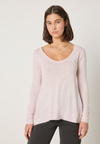 Svijetloružičasta majica s dugim rukavima, V-izrezom i ležernim krojem. Izrađena od mekane, teksturirane tkanine s blago produženim stražnjim dijelom.