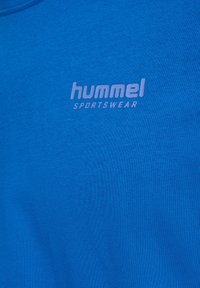 Niebieska tkanina sportowa z białym logo "hummel SPORTSWEAR" nadrukowanym na okolicy klatki piersiowej.