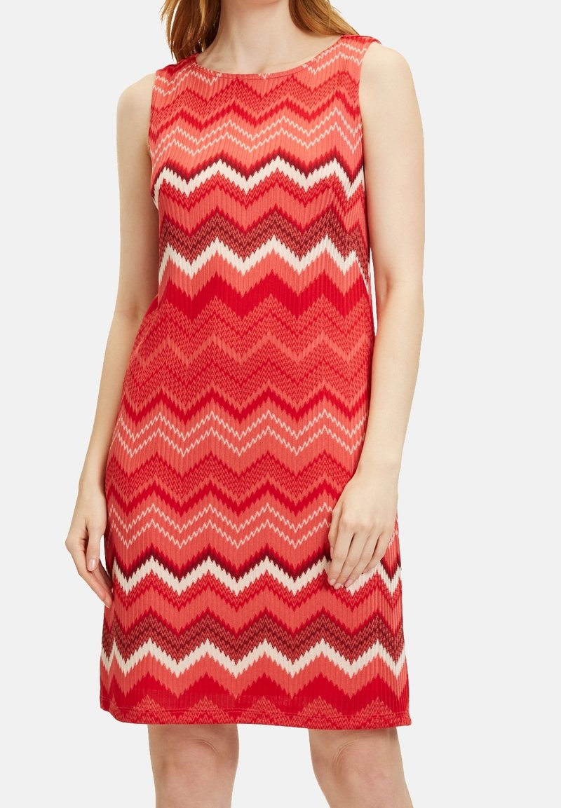 Czerwona sukienka bez rękawów z wzorem w zygzak w różnych odcieniach czerwieni, bieli i ciemnego brązu; wykonana z lekkiego materiału.