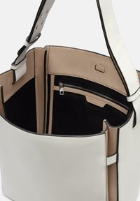 Sac fourre-tout en cuir blanc au design structuré, avec un intérieur beige, des accents noirs, une poche zippée et une sangle plate.