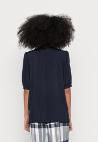 Blusa blu navy con maniche a palloncino corte, tessuto leggero, leggera arricciatura sul retro, abbinata a pantaloni a righe.